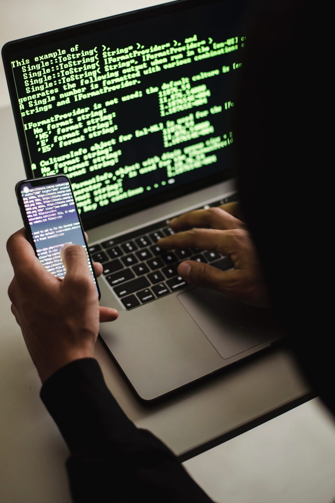 Unrecognizable hacker with smartphone typing on laptop at desk Stock Photo