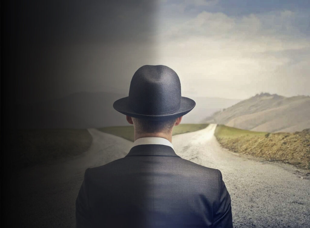 Drawing of a man in a suit and bowler hat from behind facing a fork in the road. The left half of the image is dark and shaded while the right side is sunny and bright.